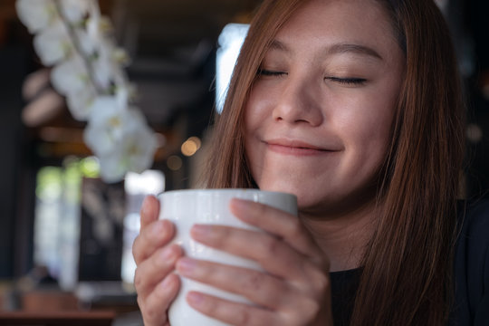 Closeup image of Asian woman close her eyes to smelling and drinking hot coffee with feeling good in cafe