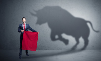 Businessman standing with red cloth in his hand and big bull shadow on the wall
