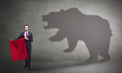 Businessman standing with red cloth in his hand and big bear shadow on his background
