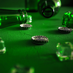 Conceptual beer background. Green beer bottles with ice cubes and lids on a green background