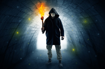 Ugly man with burning flambeau walking in a dark tunnel