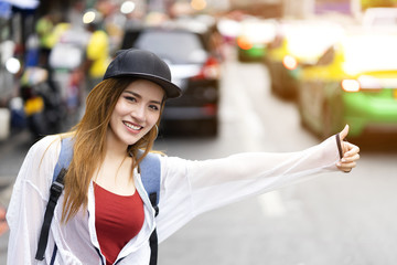Young attractive woman backpacker call taxi on busy street at Chinatown, Bangkok, Thailand with feeling happiness, cheerful, enjoyable. Traveler traveling alone with bag in summer with cars background
