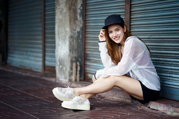 Young Asian traveler woman sitting on site walk with black cap during walking in China Town in Thailand. Attractive woman portrait in outdoor with smiling face and happiness emotional