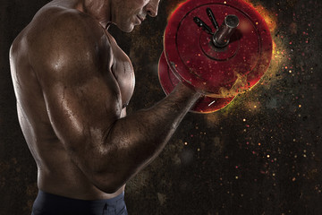 Athletic man training biceps at the gym with fire effect