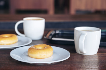 Two set of donuts in a white plate with coffee cups on wooden table
