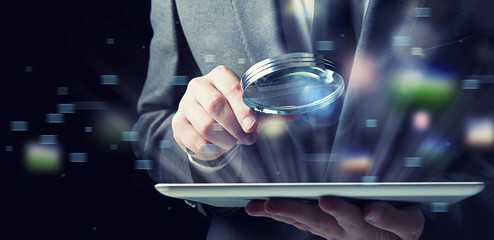 Businessman examines a tablet with a magnifying glass. Concept of internet security