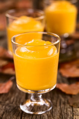 Hausgemachte Kürbismousse oder -pudding in Gläser, fotografiert auf rustikalem Holz (Selektiver Fokus, Fokus auf den vorderen Glasrand des ersten Desserts)