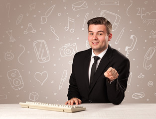 Young handsome businessman sitting at a desk with white mixed media icons behind him