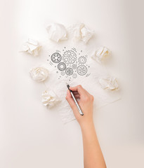 Female hand next to a few crumpled paper balls drawing rotating gears