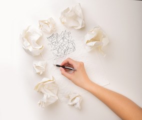 Female hand next to a few crumpled paper balls drawing random scribbles 