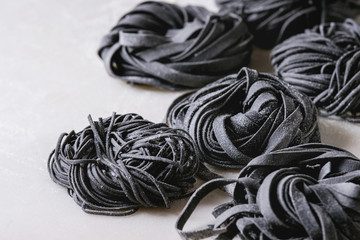 Variety of italian homemade raw uncooked cuttlefish ink black pasta spaghetti and tagliatelle with semolina flour on white marble table. Close up.