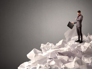 Thoughtful young businessman standing on a pile of crumpled paper with a deep grey background