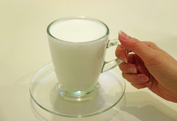 Female's hand holding a Cup of Warm Milk Served in Transparent Glass Cup 