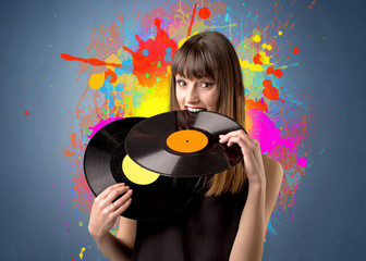 Young lady holding vinyl record on a grey background with colorful splashes behind her 