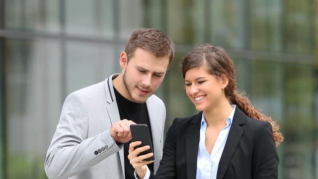 Two businesspeople watching and talking about smart phone content in the street