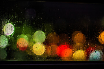 Blurry city lights can be seen through a window, with rain drops visible