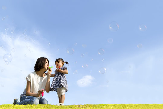 公園で青空バックにシャボン玉をして遊ぶ幸せな親子。家族、親子、幸せ、愛情、育児、健康イメージ