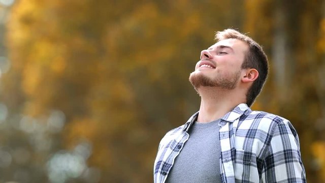 Happy man breathing deep fresh air in a park in autumn with trees in the background