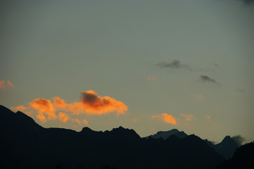 Dawn over mountains. The sun illuminates the silhouettes of mountains and clouds at dawn. Over the peaks are visible sunbeams