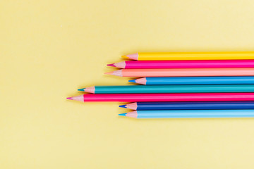 Color pencils in a row on yellow background.