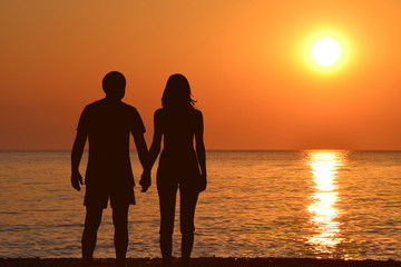 Young couple holding hands watching a sunrise at seashore