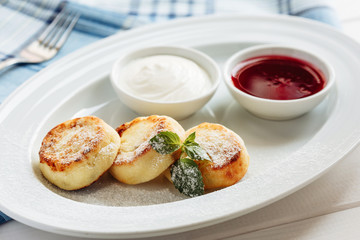 Summer cottage cheese pancakes on white plat on a wooden table with sour cream, mint and jam, closeup, selective focus