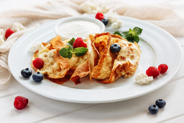 closeup of pancakes with cottage cheeseand strawberry, blueberry on plate on white plate background, decorated with mint leaves