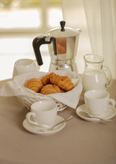 Fototapeta na wymiar Coffee maker, cups and croissants in the basket are on a round table in front of the window.
