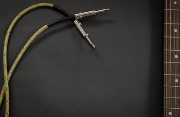 Background with fretboard of an electric guitar and a vintage Jack cable for amplifier on black...