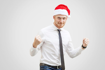 Happy handsome businessman in white shirt, black tie and red new year hat, looking at camera with smile and celebrting with raised arms. . indoor studio shot, isolated on light gray background.