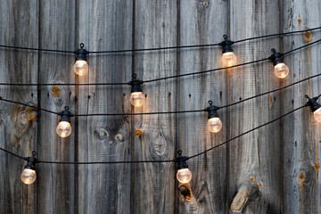 String of lights, yellow bulbs on old wooden background in the garden, copyspace, patio lighting decoration concept