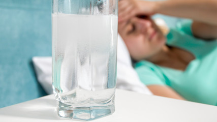 Closeup image of aspirin in water against woman suffering from headache
