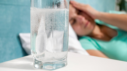 Image of glass of water with aspiring and young woman suffering from headache lying in bed