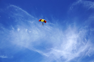 Multicolor red-yellow parachute with silhouettes of skydivers against the background of a clouds...