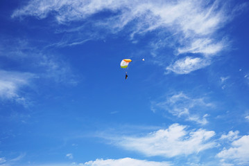 White-orange parachute canopy of tandem is flying against the background of a lighty clouds