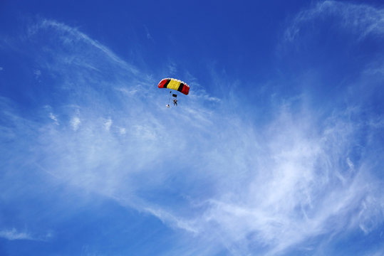 Multicolor red-yellow parachute with silhouettes of skydivers against the background of a clouds and blue sky.