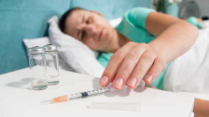 Closeup photo of young sick woman taking syringe with painkiller medicine from bedside table