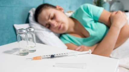 Closeup image of syringe with medicines and sick woman lying in bed