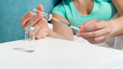 Closeup image of young woman lying in bed and preparing syringe for injection