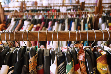 Wooden clothes racks with hangers and with colorful clothes inside a shop. - obrazy, fototapety, plakaty