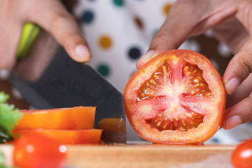 Cook is cutting fresh red tomatoes to cook
