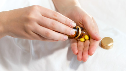 Closeup photo of woman pouring tablet on hand from glass bottle
