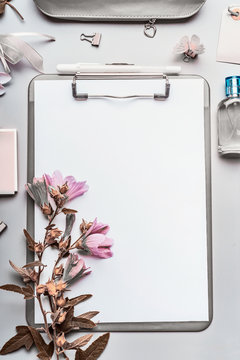 Modern business female desktop background with gray clipboard, blank paper sheet , perfume, office tools and accessories and flowers. Top view, flat lay.  Instagram style