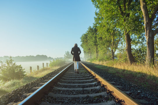 Einzelne Frau läuft auf Bahnschienen dem Horizont entgegen.