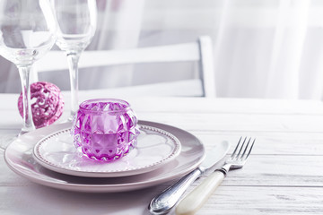 Purple Christmas table setting with candlestick and glasses of wine above light window and chair on wooden background