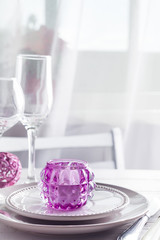 Purple Christmas table setting with candlestick and glasses of wine above light window and chair on wooden background