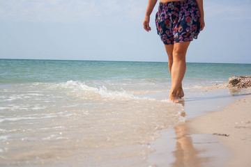 Woman legs are walking along the picturesque seashore with aquamarine colour sea water at the background