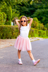 Fashionable little girl smile in sunglasses on the street. Vertical photo