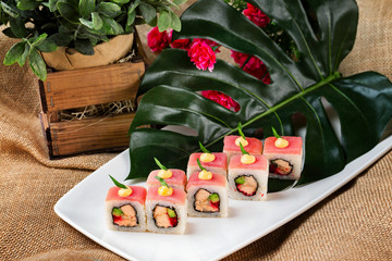 Plate of sushi rolls with tuna, avocado, salmon decoratyed with flowers at sack cloth background.