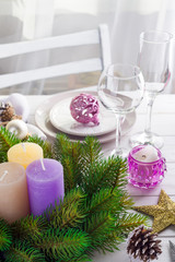 Obraz na płótnie Canvas Christmas wreath with colorful big candles on a table with a Christmas table setting on a white wooden table in front of a light window